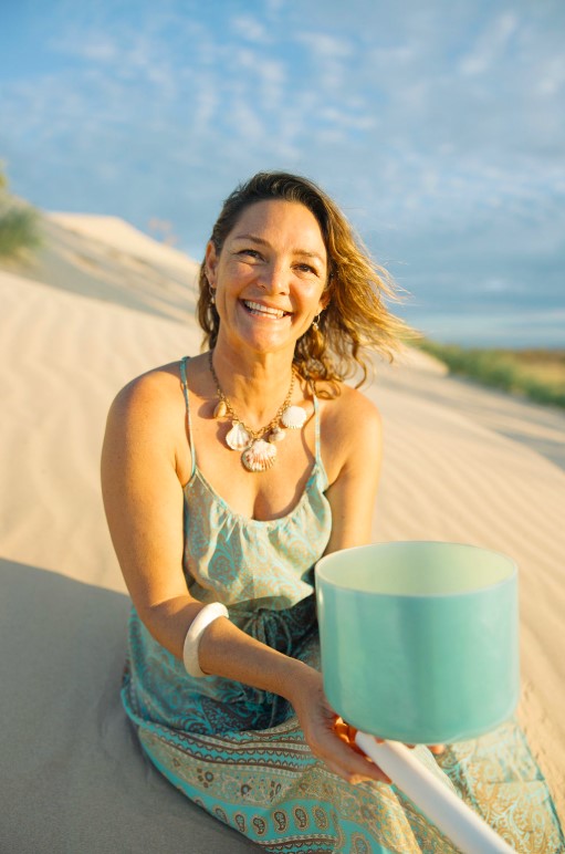 Naomi smiling, sitting on a sand dune, golden hour, with a crystal bowl
